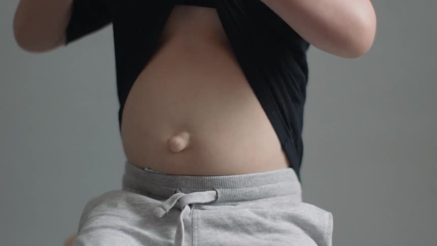 A little boy is pulling his shirt up to show his stomach