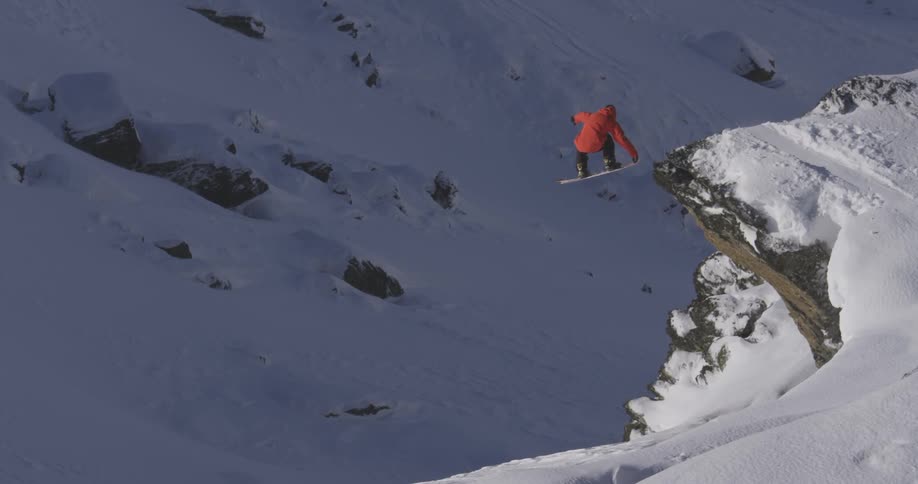 A snowboarder jumps off a cliff