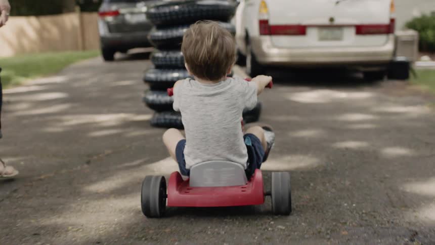 A kid is riding on a tricycle with his mom walking next to him