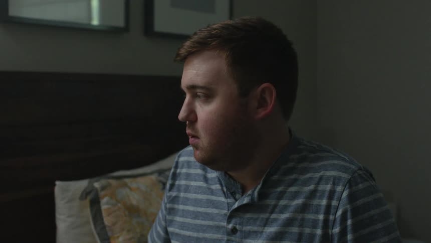 Depressed looking man sits on a bed