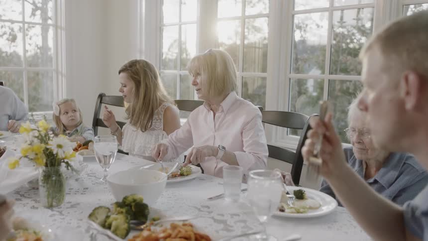 Family sits at a dinner table as they talk and eat