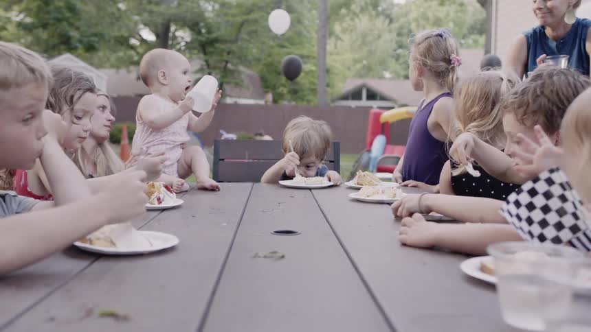 Several children sitting at a picnic table in a backyard