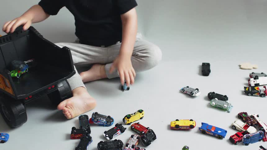 A young boy plays with hot wheels and a dump truck