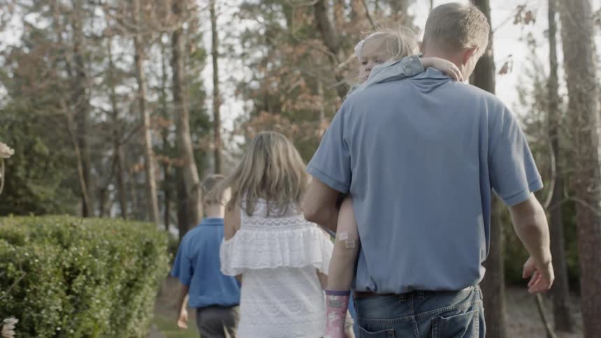 Man carries a little girl as he walks in the forest with his family
