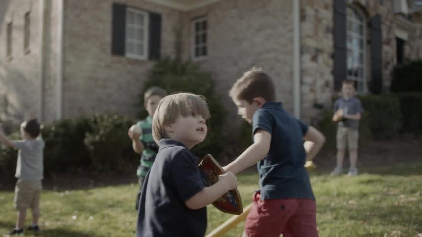 Young boy holds a bat as he runs around another young boy