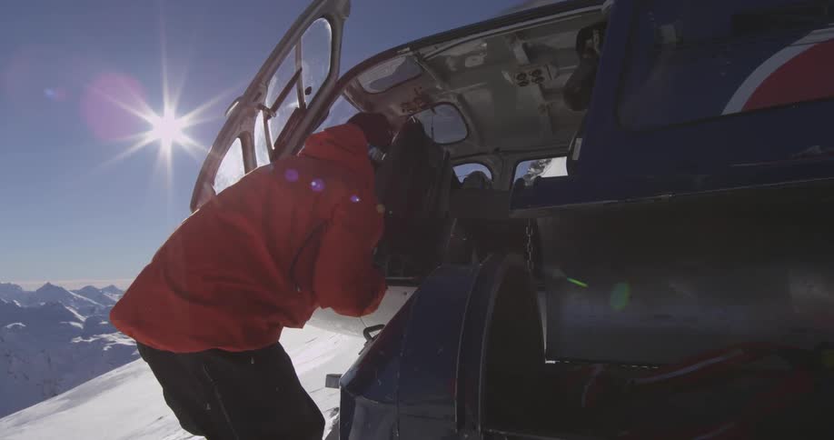 A man exiting a helicopter on a snow covered mountain on a sunny day