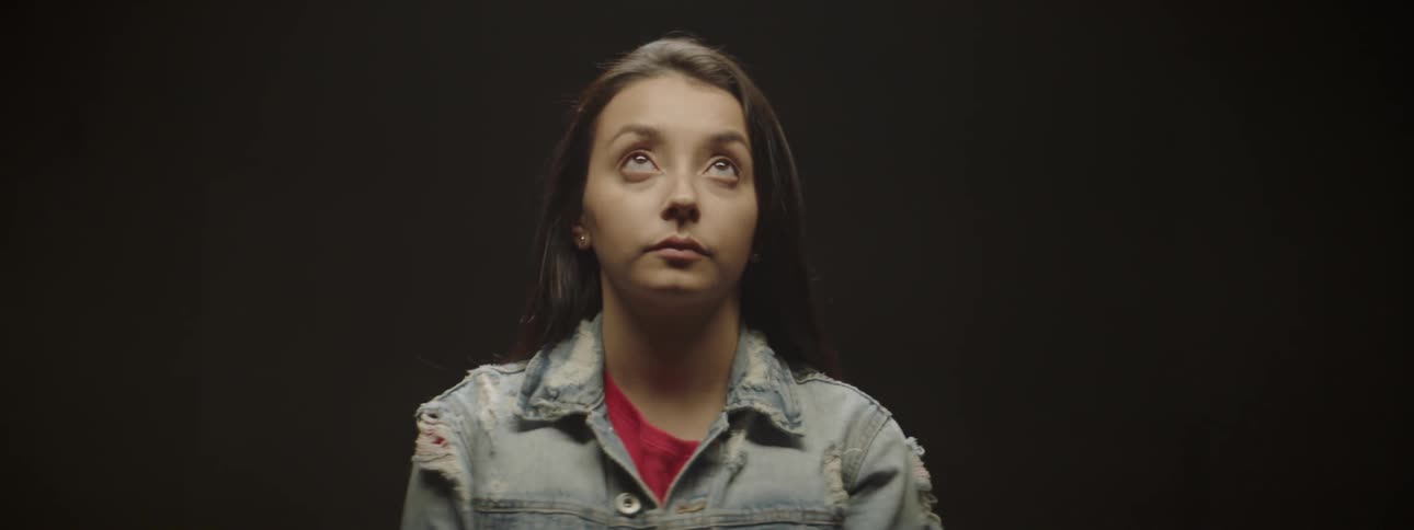 Woman standing in a dark room opens her eyes and looks up at light