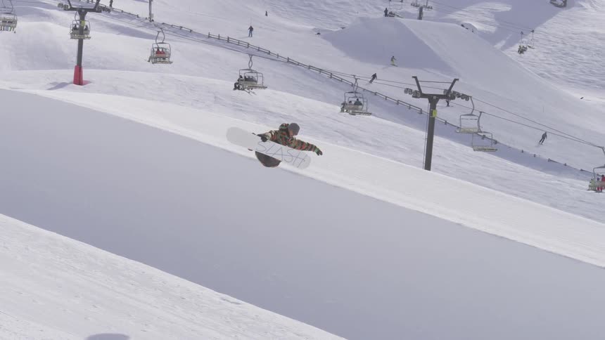 People riding a ski lift and a snowboarder performing a jump on a mountain