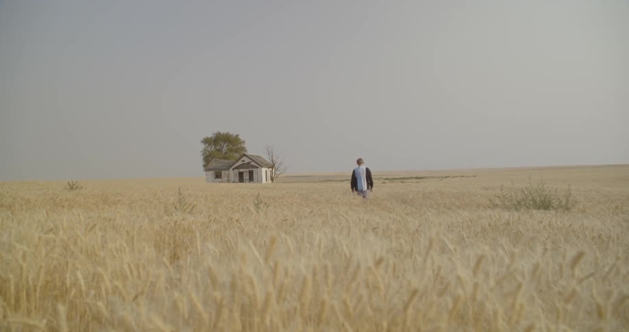 Man walks across a grassy field toward an abandoned house