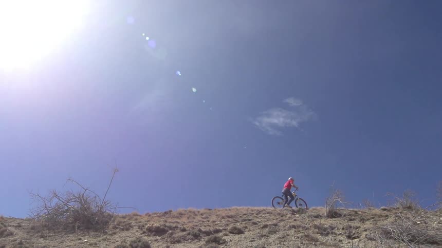 A bicyclist walks on a sunny hill