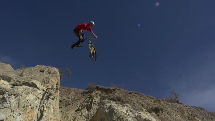 A young man jumping his bike from one steep cliff to the next