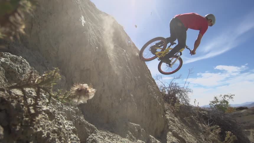 A man jumps his mountain bike onto a rock and rides over the rock and back down the hill