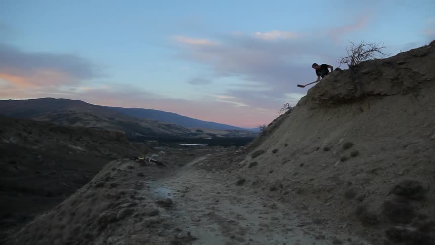 A person patting down the soil above a narrow mountain road