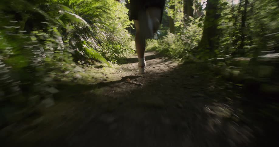 Man runs on a dirt path through the trees on a sunny day