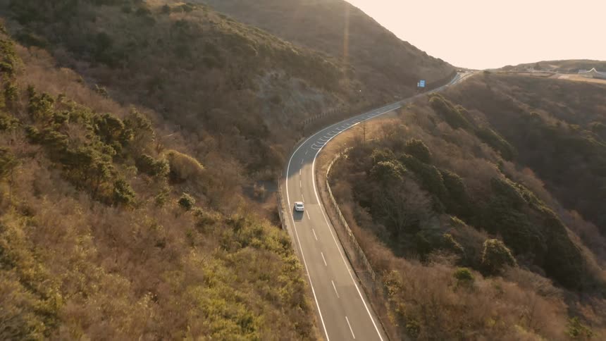 A car is driving on a country road in daylight