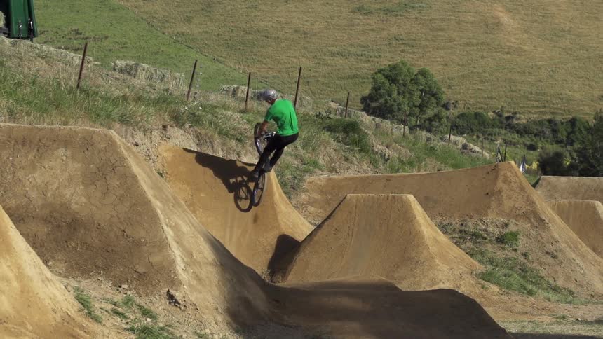 Man riding a bike and jumping off some dirt hills on a sunny day
