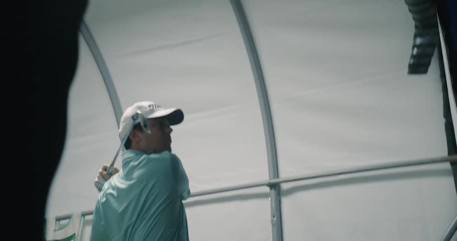 Man practices hitting a golf ball inside a tent