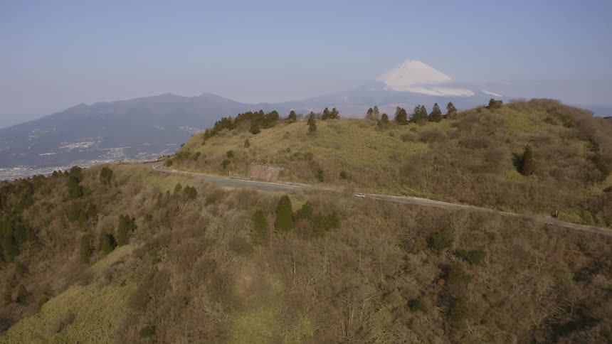 A car travels on a road that winds around the top of a hill