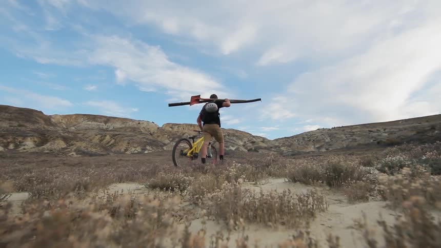 A man walks a bicycle through the desert