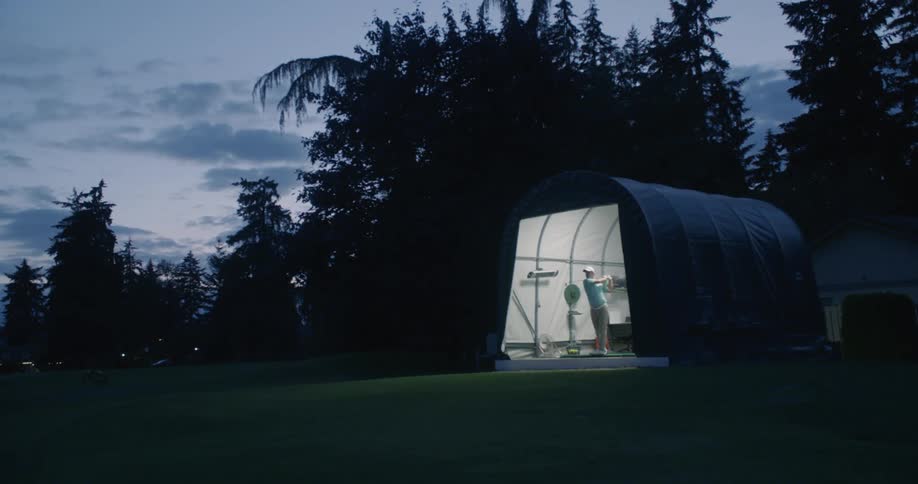 A man is practicing his golf swing at dusk