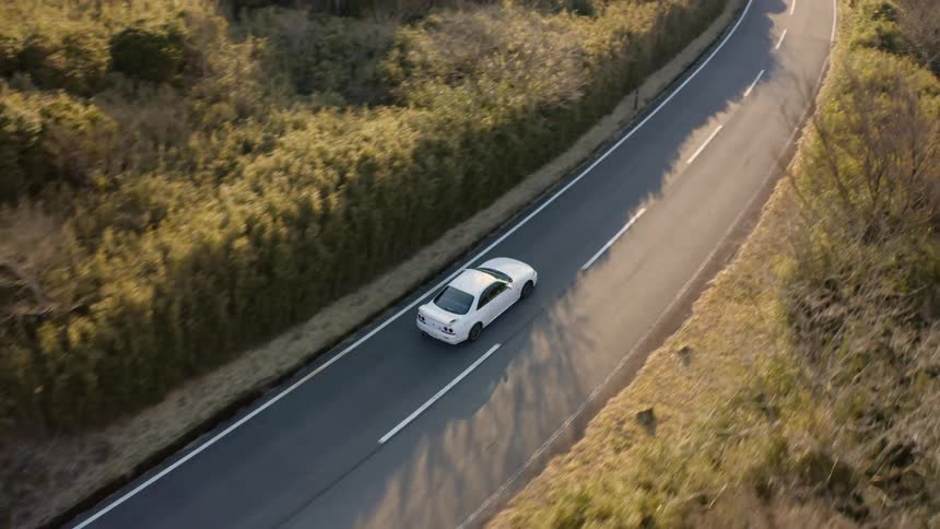 A car is driving on a country road in daylight