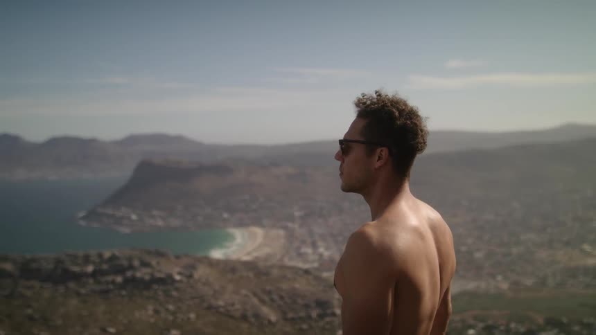 A man stands on top of a hill overlooking the shore