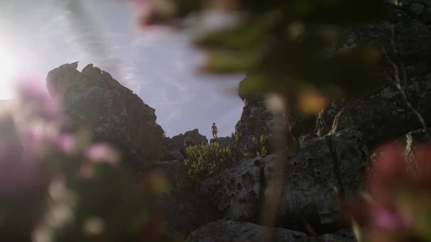 Sunlight is pouring over a cliff ledge as a person stands on top taking in the view