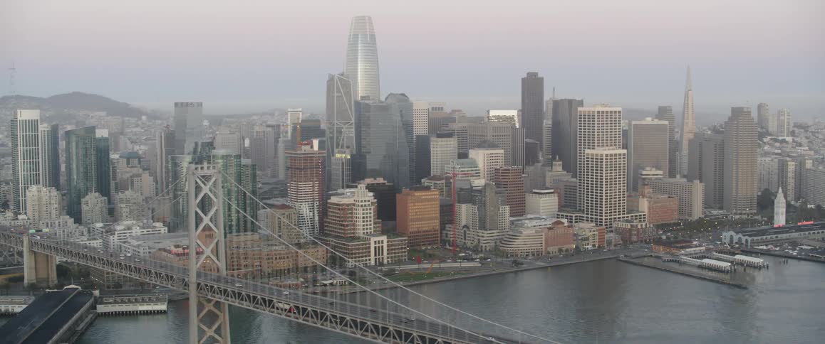 Traffic is crossing a bridge into a city in daylight