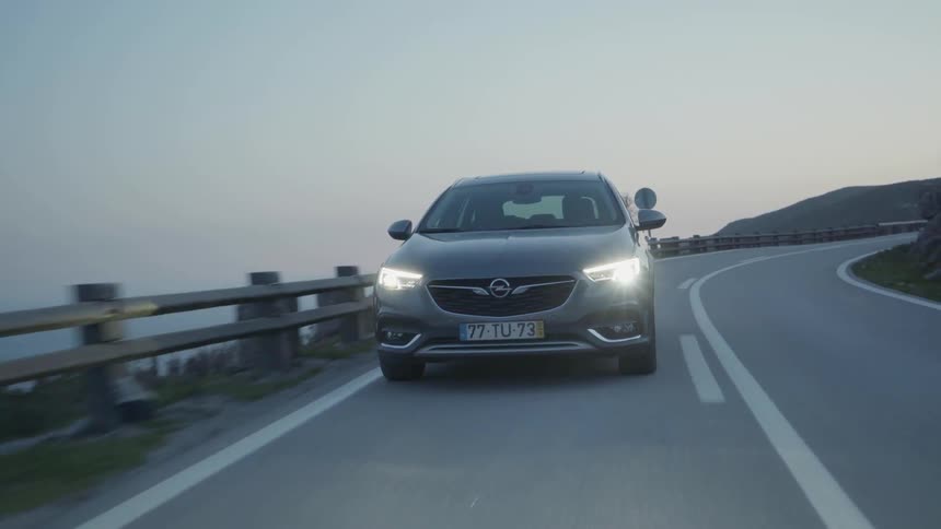 A car drives around the bend of the road by the water
