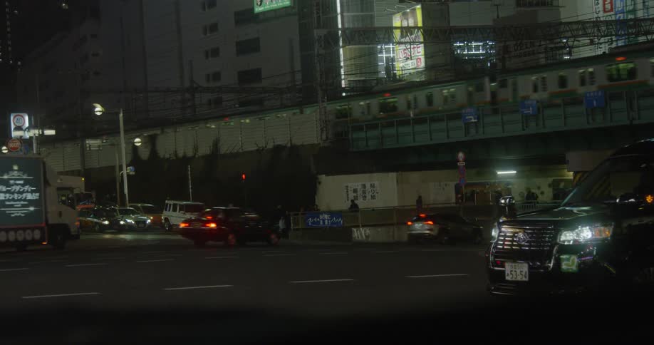 Vehicles driving in Tokyo street at night with a train on a bridge overhead