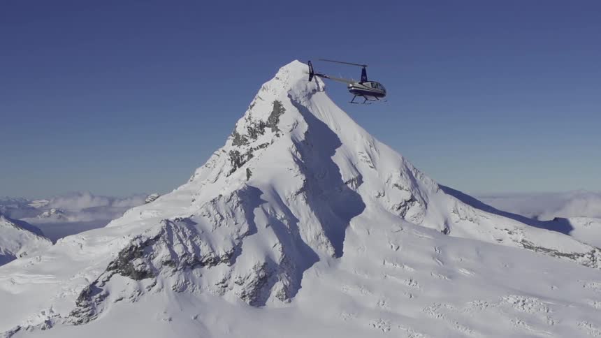 Helicopter flies close to a snow covered mountain peak