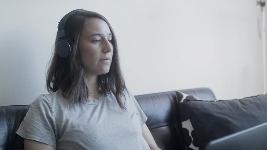 Woman looks at a laptop while wearing headphones and sitting on a couch
