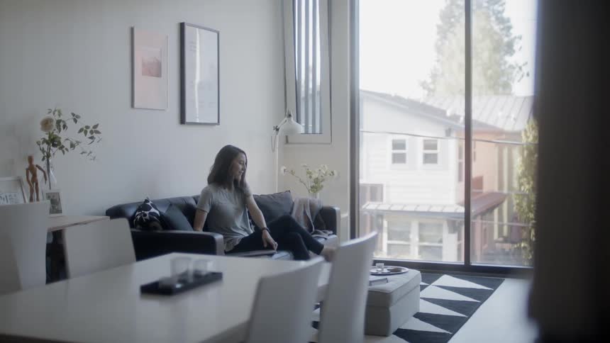 A woman is sitting down and opening a laptop on her couch during the day
