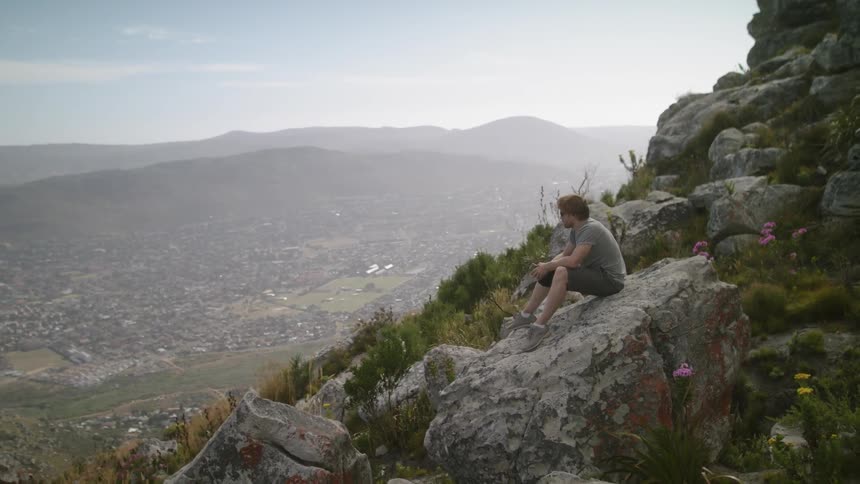A man sits on a large rock on the hill