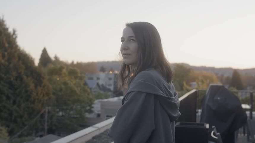 Woman smiles as she looks to her left from a balcony
