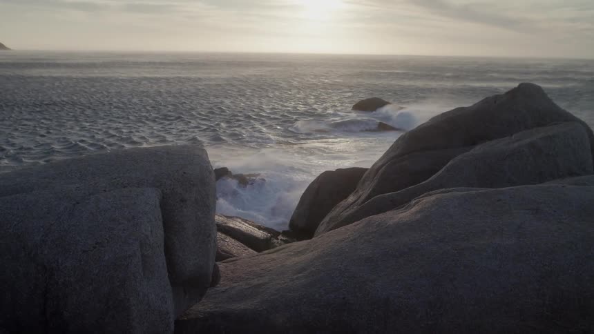 Ocean waves splash against the rocks at sunset