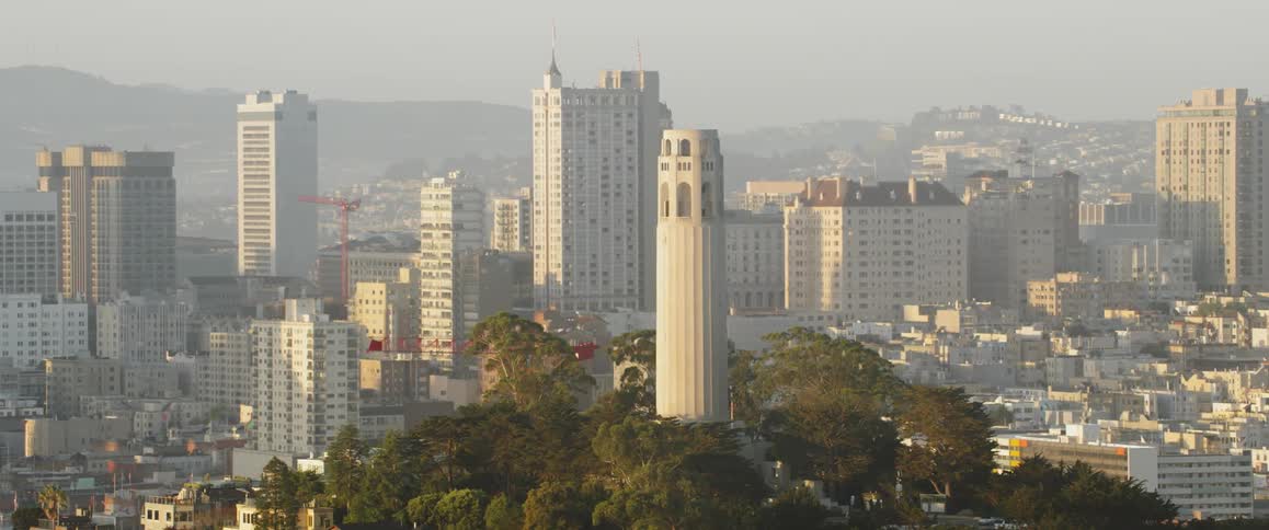 A construction crane is operating near coit tower on a hazy day