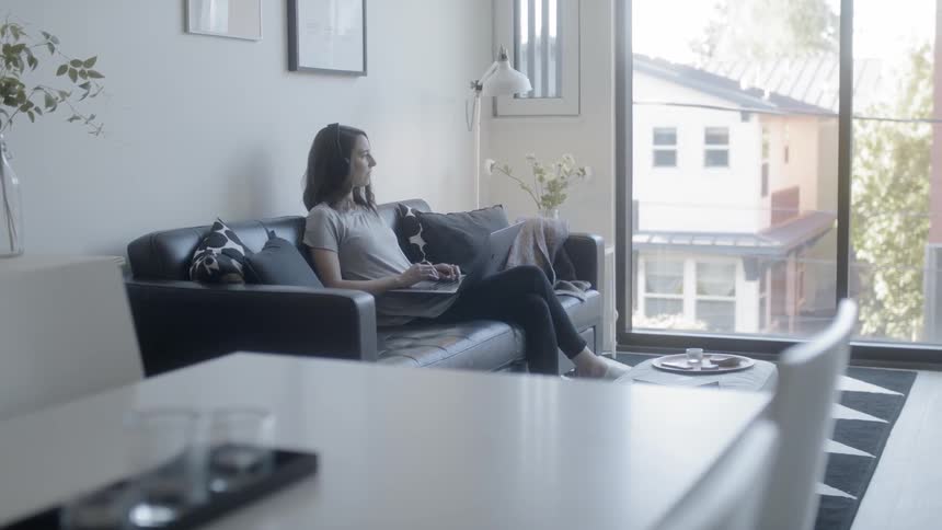 A woman sits on a couch and works on a laptop