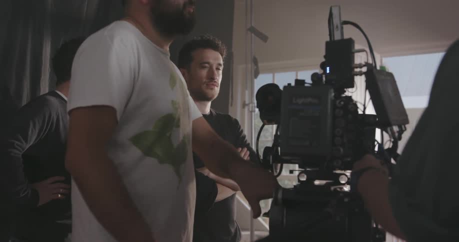 A man controls a tv camera on set while others stand by