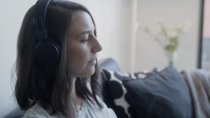 A woman with headphones on sits on the couch and calmly listens to music