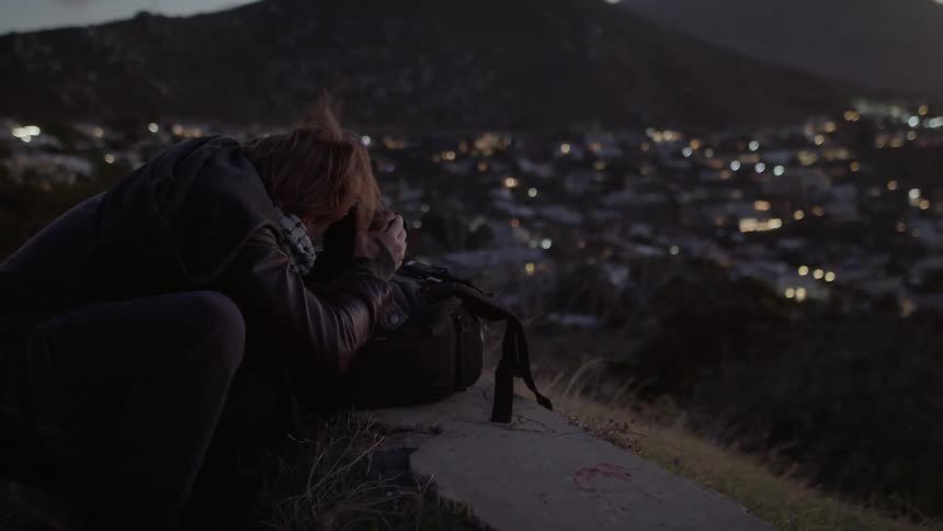 Man is photographing city from lookout on windy night