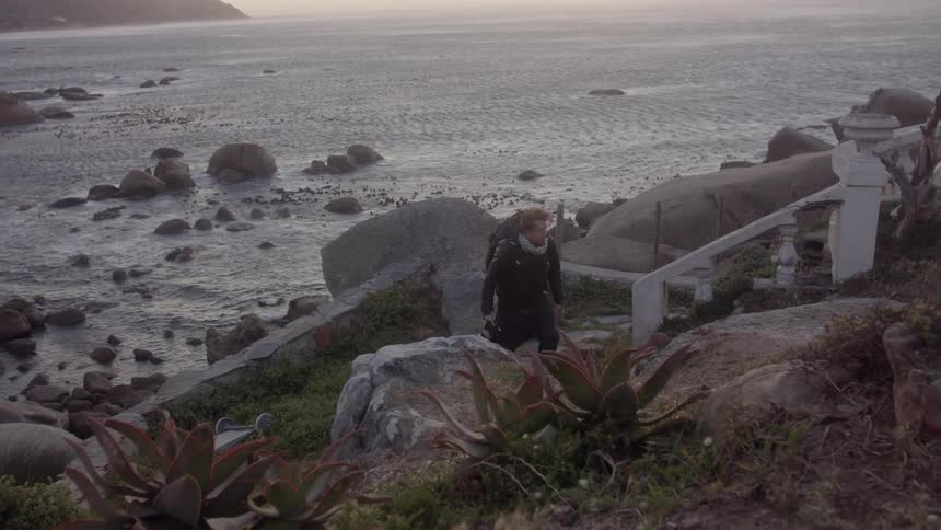 A person walks up the rocks of the shore with a camera