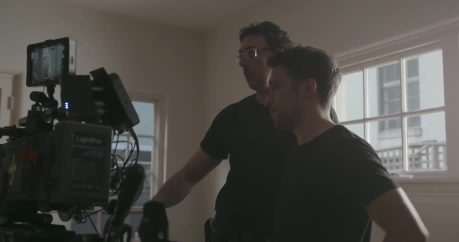 Men in a room talk and gesture near a tv camera