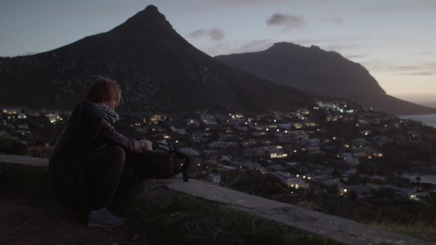 A man adjusts his camera on a bag overlooking a village below