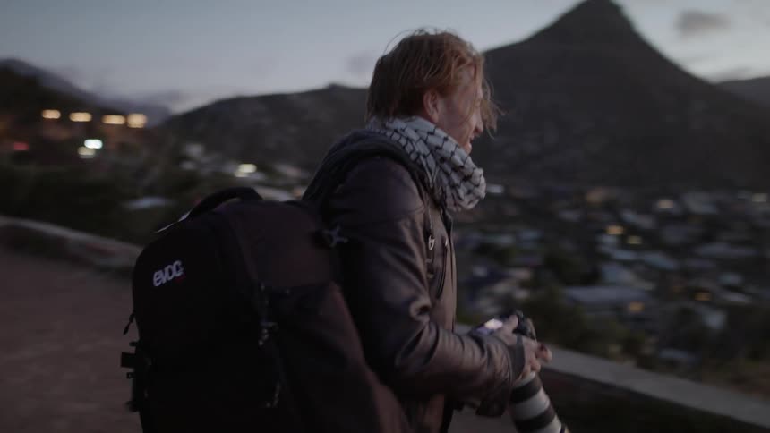 Man carries a camera as he wears two backpacks