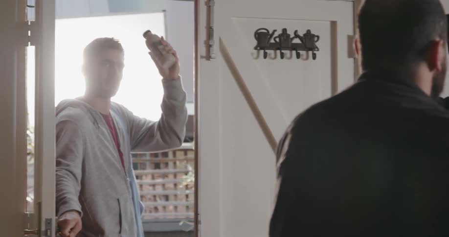 Man turns a video camera around as a man tosses him a bottle