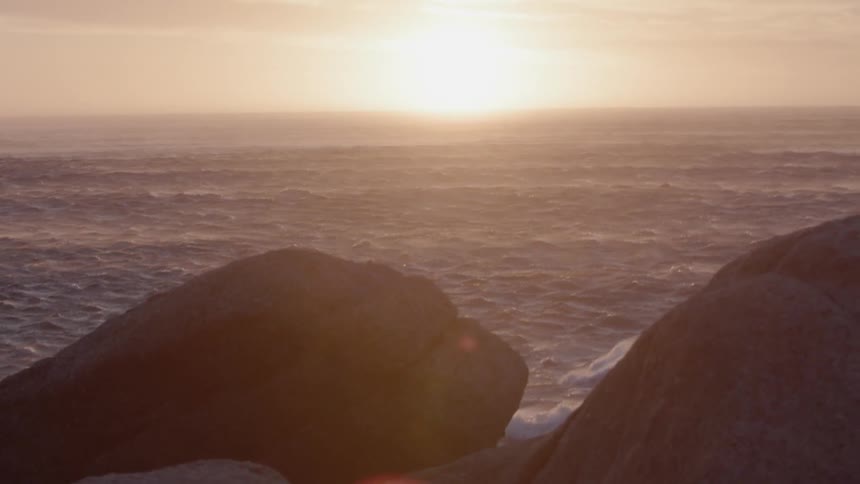 Ocean waves splash against the rocks at sunset