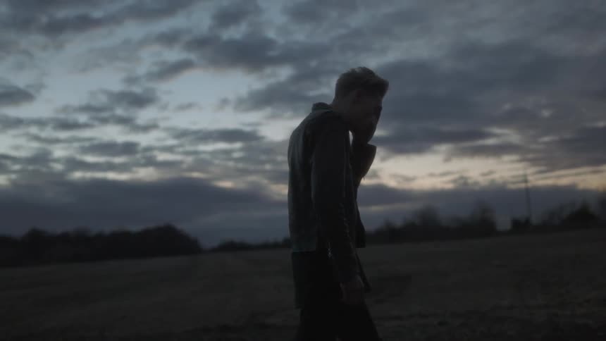 A man walking in a field at sunset looks up at the cloudy sky