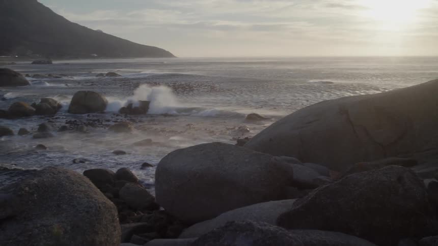 Waves crash into the rocks under a cloudy blue sky