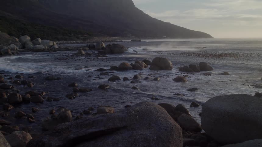 Waves crash around the rocks under a cloudy sky